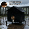 A black elevated floor stand cat shelter with an entrance, shown outdoors in the rain.