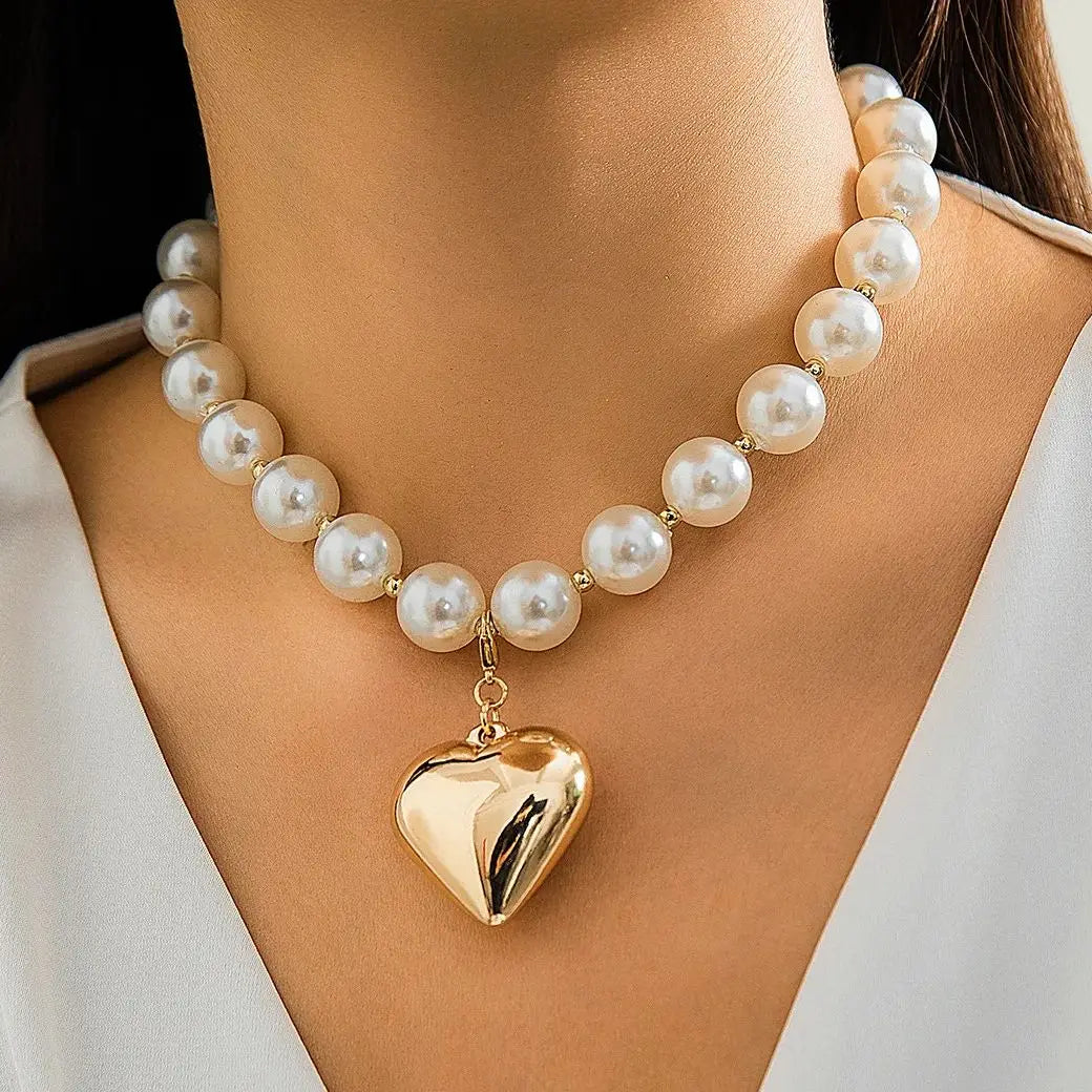 A close-up of a pearl choker necklace with a heart pendant worn around the neck.