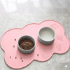A pink non-slip pet mat holds a small bowl of dry food and a separate bowl of liquid food.