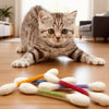 A kitten is lying on a wooden floor next to a set of soft, fuzzy catnip toys.