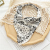 A white and black bohemian paisley triangle scarf draped on a beige fabric background.