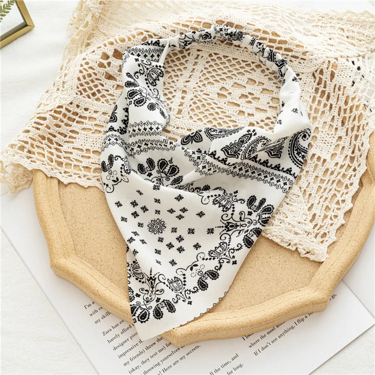 A white and black bohemian paisley triangle scarf draped on a beige fabric background.