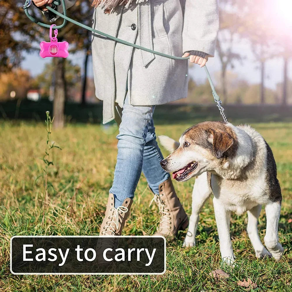 A person is holding a green leash attached to a pink reusable pet poop bag dispenser, with a dog standing nearby.