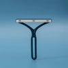 A teal manual lint remover brush with a silver bar is shown against a solid blue background.