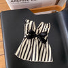 A striped black and white pet dress with a black bow displayed on a black surface.