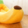 A yellow banana-shaped plush pet bed with a brown tip, resting on a wooden surface.