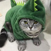 Un gato atigrado vistiendo un mono de disfraz verde con orejas puntiagudas, sentado en un suelo blanco.