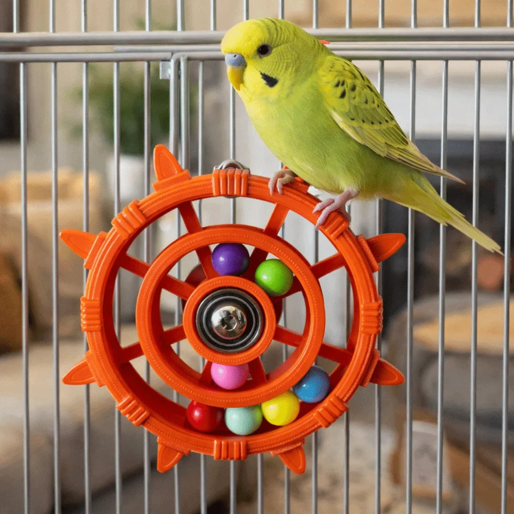 Ein gelbes Vogel sitzt auf einem orangefarbenen, rotierenden Rasseltspielzeug in einem Drahtkäfig.