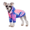 A small dog wearing a tie-dye fleece hoodie featuring shades of pink, blue, and purple.