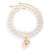 A delicate choker necklace made of small white pearls with a gold chain and a heart-shaped pendant.