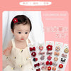 A close-up photo of a baby wearing a white outfit, with several pink and red flower-shaped hair clips displayed in a packagin