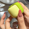 A hand holds a lime green portable lint roller for pet hair removal against a blurred background.