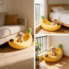 A yellow banana-shaped plush pet bed with green accents is shown for a dog in a bright room.
