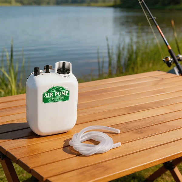 A white portable air pump labeled AIR PUMP for aquarium and fish tank oxygen resting on a wooden table near water.