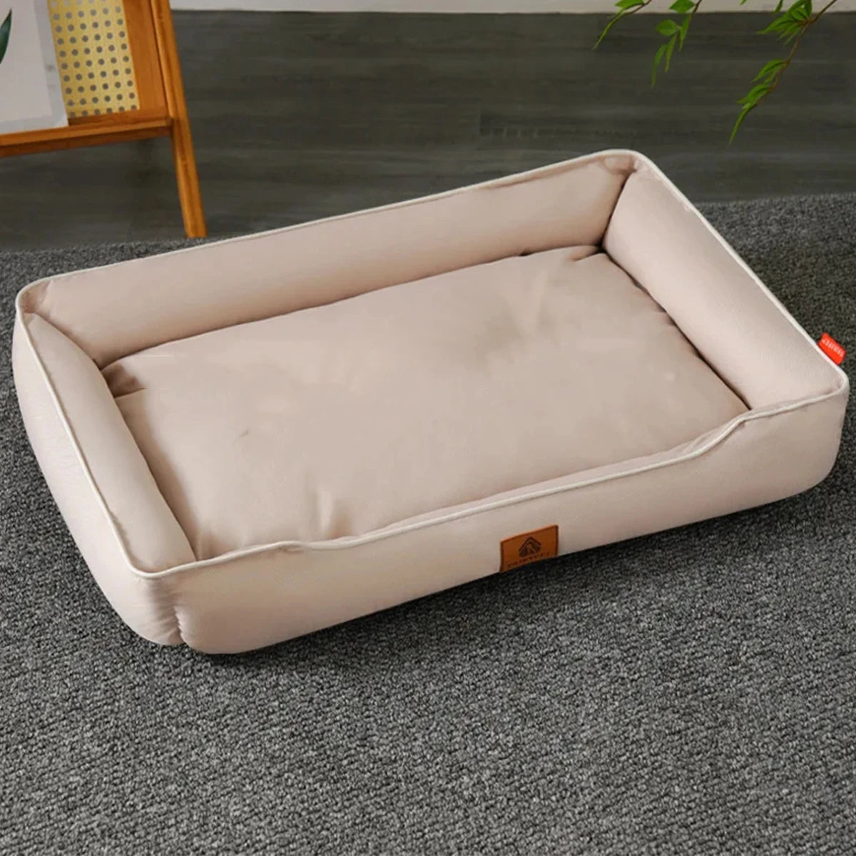 A beige waterproof orthopedic dog bed with a removable cover resting on a gray carpet.