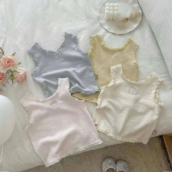 Three light colored mini vests for baby girls with lace trim and embroidery displayed on a white surface.