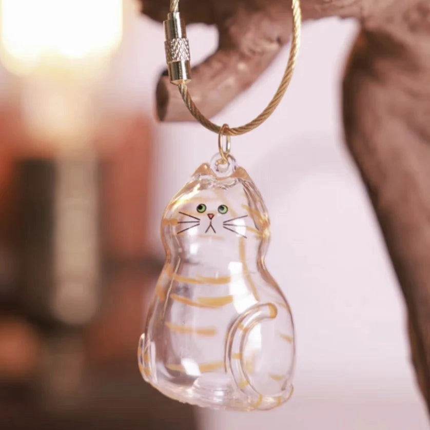 Klare Glasfigur einer orangefarbenen Katze hängt an einem goldfarbenen Schlüsselanhänger.