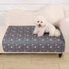 A fluffy white puppy is lying on a gray pet pad in front of a cream-colored sofa.