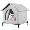 A gray insulated cat house with a pitched roof and an entrance, featuring a cat looking out.