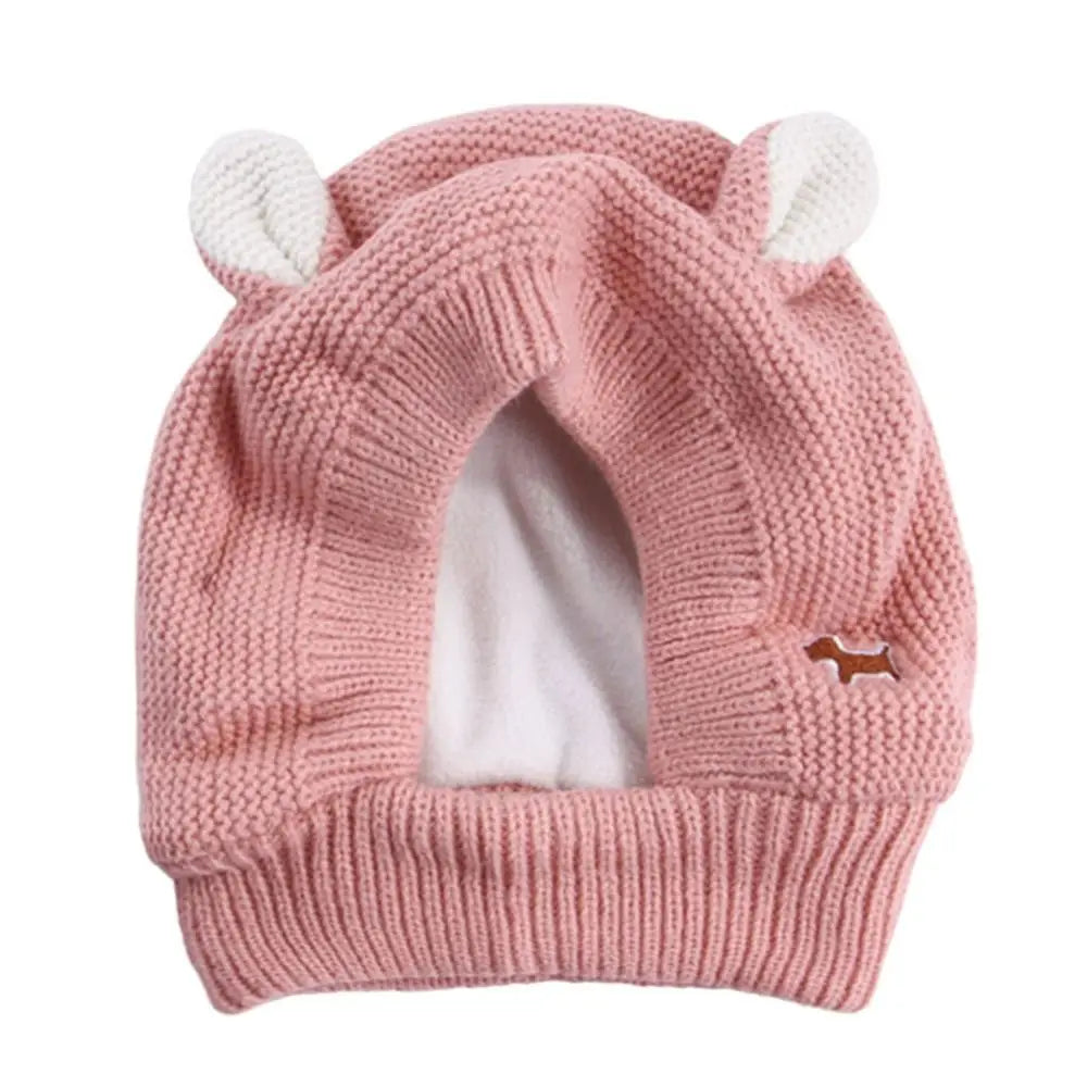 A pink knit beanie with white ear muffs for dogs