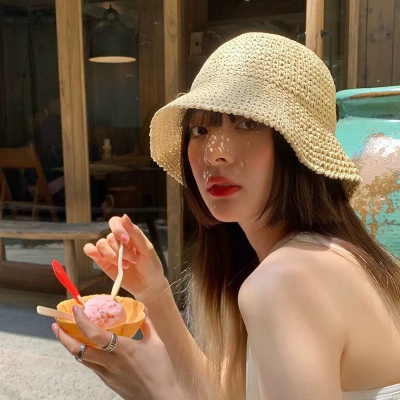 Une femme portant une casquette pliante en paille beige tenant une glace pilée rose.