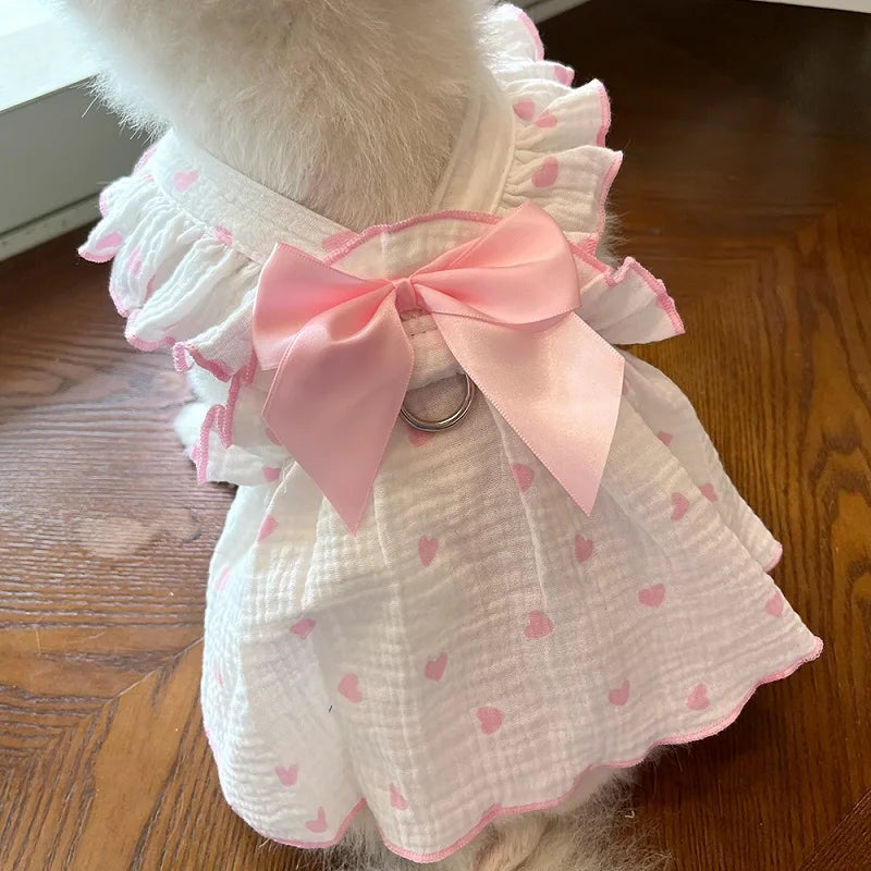 Une robe de chien blanche avec des bordures de volants roses et un nœud rose, portée par un chien de couleur claire.