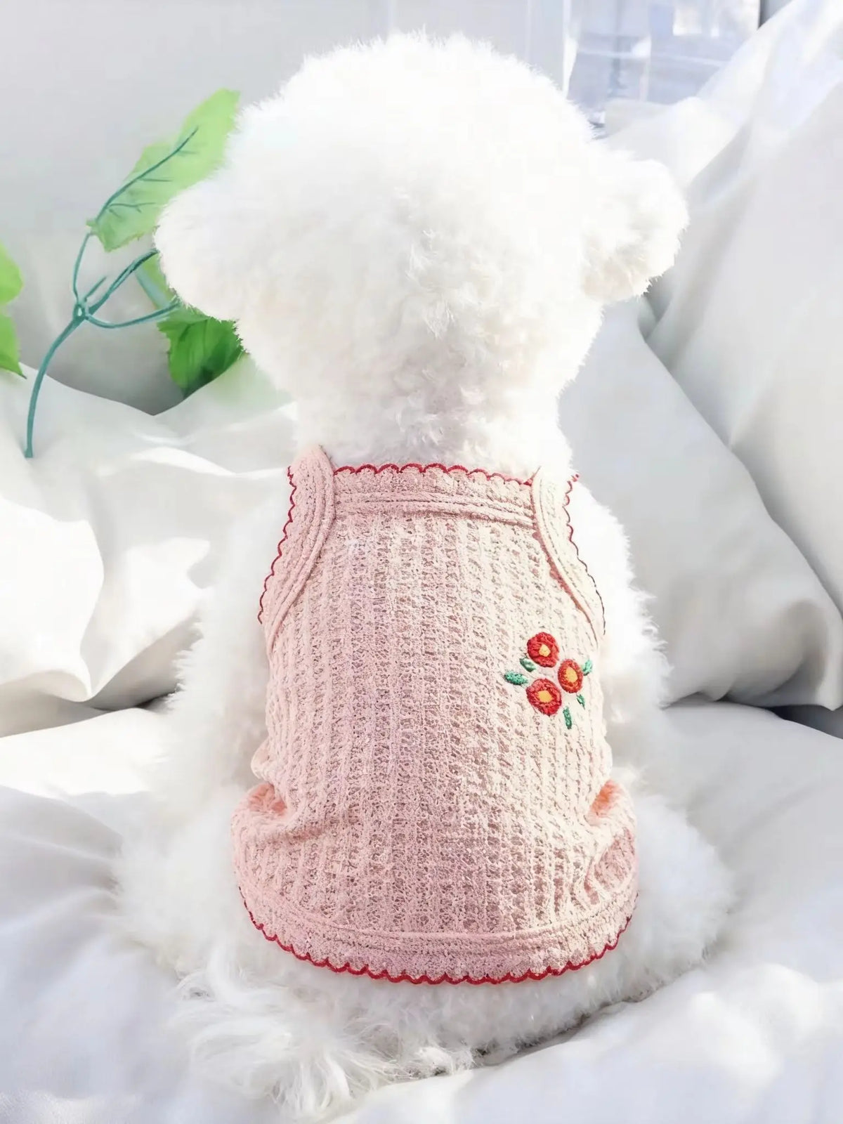 Un collar de mascota blanco y esponjoso con textura de punto rosa y ribete rojo, sobre ropa de cama blanca.