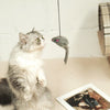 A fluffy gray and white cat looks up at a long, thin stick with a small pink toy dangling from the end.
