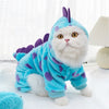 A fluffy white cat wearing a bright blue dinosaur fleece hoodie with purple accents.