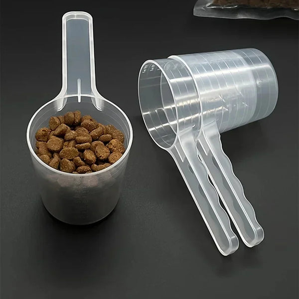 A transparent pet measuring spoon with a scale for dog and cat food is shown next to a container of kibble.
