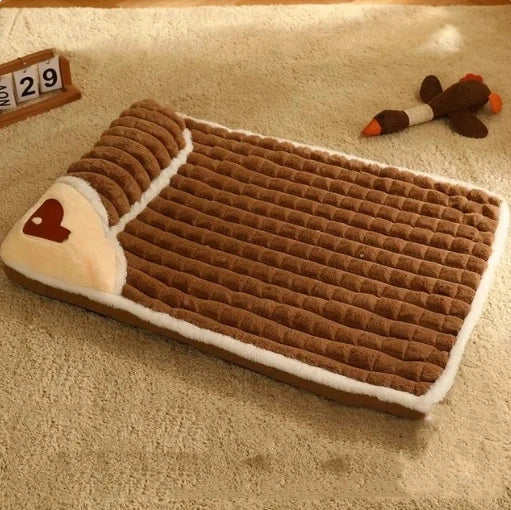 A brown orthopedic memory foam dog bed with light tan trim and a small brown heart patch resting on a beige carpet.