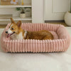 Un chien orange et blanc duveteux se détend dans un lit de chiot rose à côtes.