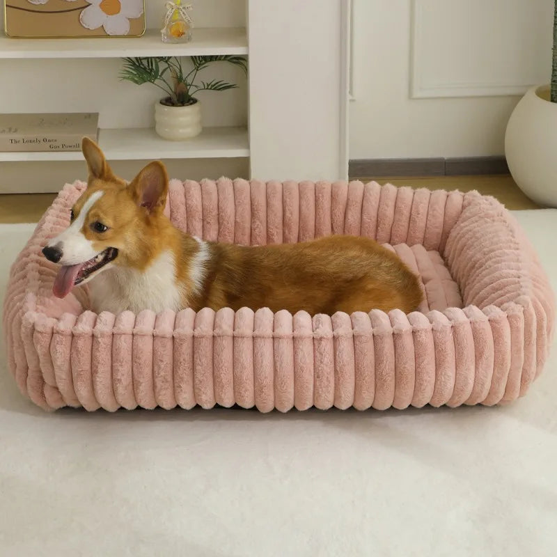 Un chien orange et blanc duveteux se détend dans un lit de chiot rose à côtes.