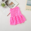 A bright pink polka dot dog dress for small breeds with a ruffled skirt, displayed on a white surface.