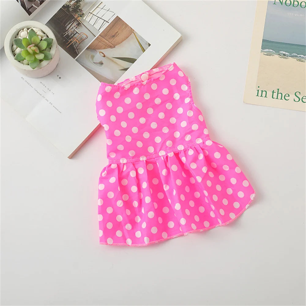 A bright pink polka dot dog dress for small breeds with a ruffled skirt, displayed on a white surface.