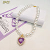A necklace featuring a strand of white pearls and a purple heart pendant, displayed on a white background.