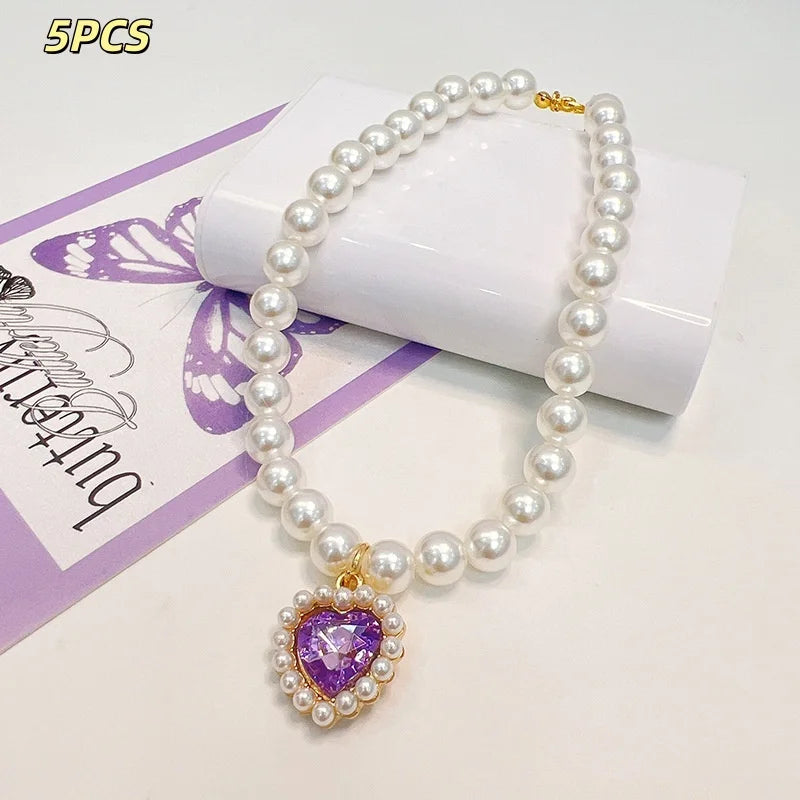 A necklace featuring a strand of white pearls and a purple heart pendant, displayed on a white background.
