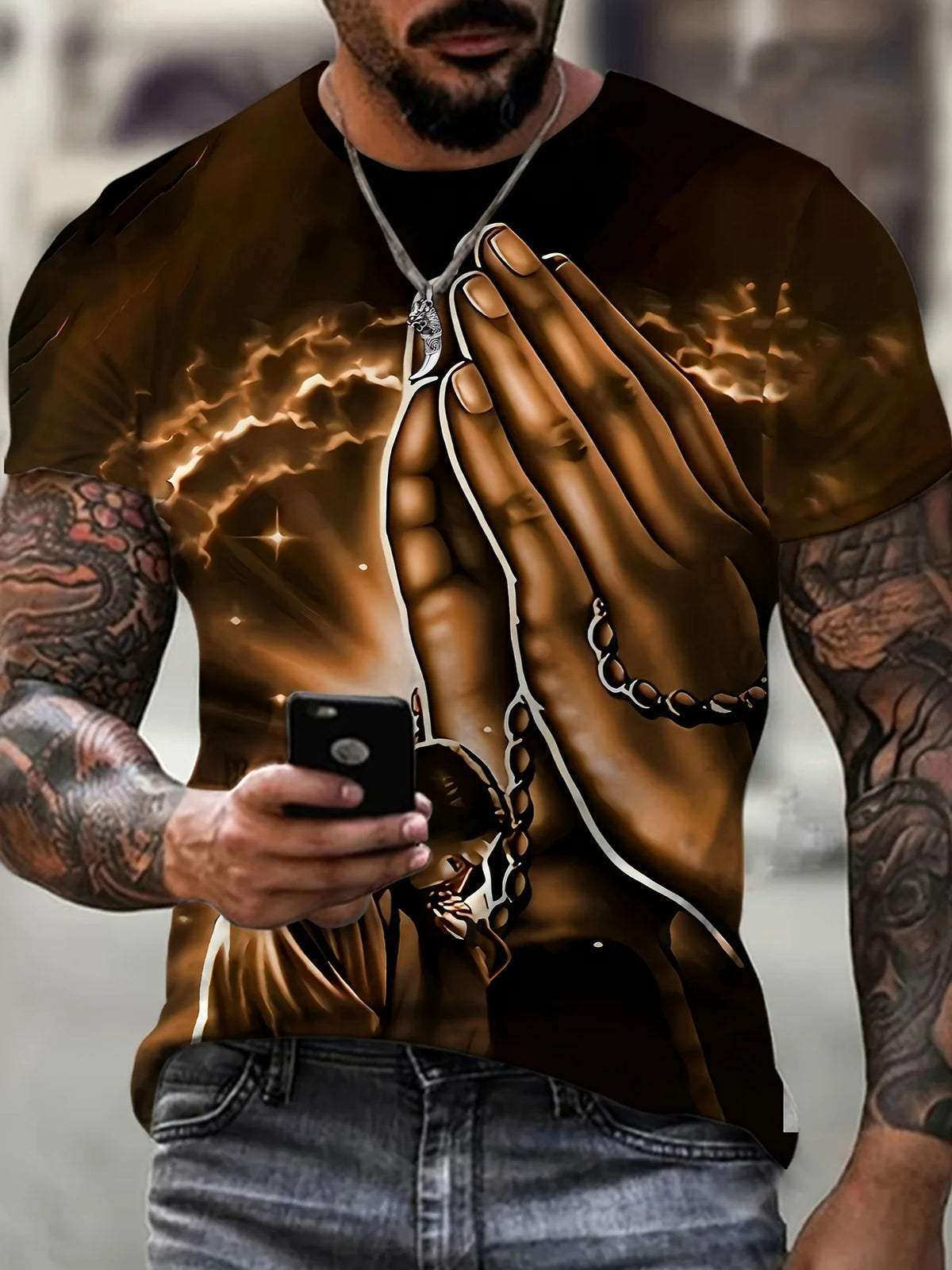 A man wearing a brown Jesus graphic print crew neck t-shirt and dark jeans, holding a smartphone.
