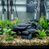 A realistic 3D printed fish tank rockery ornament featuring dark rocks and green aquatic plants.