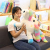 A young woman is holding a white unicorn plush toy with rainbow accents while sitting on a couch.