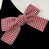 A red and white plaid fabric bow tied in a ribbon, used as hair clips.
