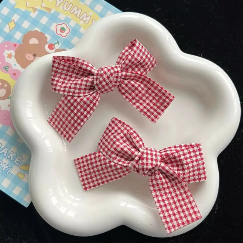 Red plaid fabric bow hair clips for girls displayed on a white dish.