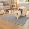 A white cat is standing on a gray honeycomb texture litter mat indoors.