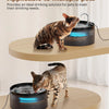 Un chat tigré boit de l'eau d'une fontaine à eau automatique sur une surface en bois.