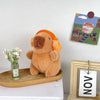 A fluffy brown capybara plush toy sitting on a wooden tray next to a framed artwork.