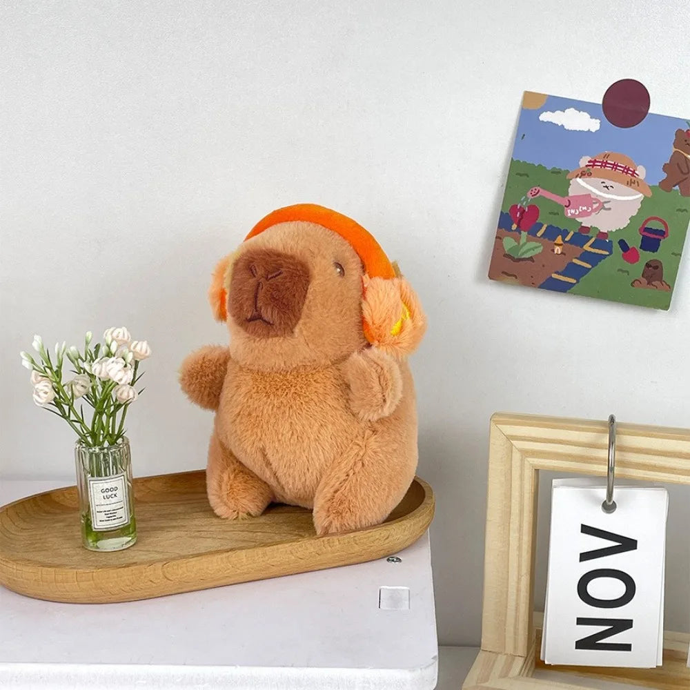 A fluffy brown capybara plush toy sitting on a wooden tray next to a framed artwork.