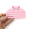 A pink reusable cat food pouch scraper shaped like a cat face is held in a hand.