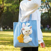 A light blue canvas pet carrier bag featuring a white cat design, being held by a person outdoors.