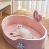 A pink pet bed with a removable cover and raised guardrail is shown, featuring a white cat resting inside.