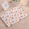 A beige fleece pet bed mat cover with a paw print pattern is displayed on a textured fabric next to a photo frame.